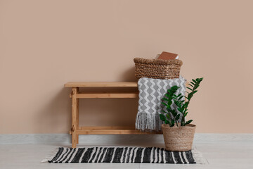 Basket with books on bench and houseplant near beige wall in room