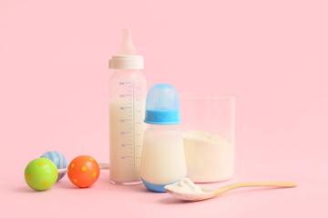 Bottles with baby milk formula and rattle on pink background