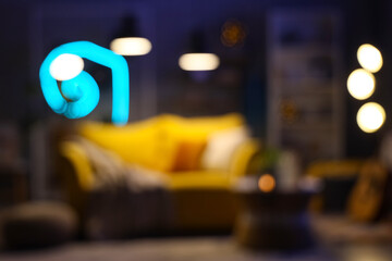 Interior of modern living room with sofa, coffee table and glowing lamps at evening. Blurred view