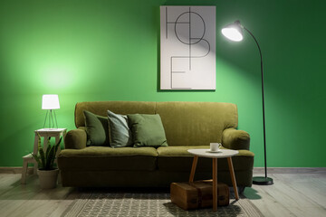 Sofa, table with cup of coffee and glowing lamps in interior of living room