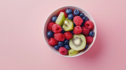 A white bowl filled with fresh raspberries, blueberries, and kiwi slices on a pink background.
