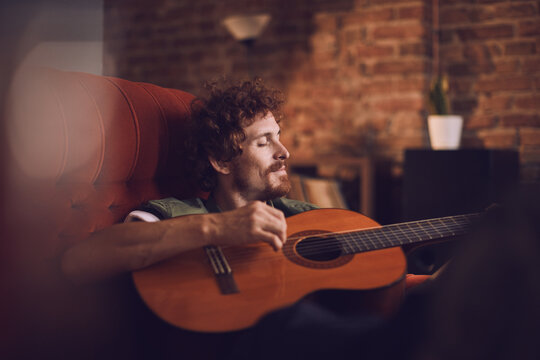 Man relaxing and playing acoustic guitar on a red couch