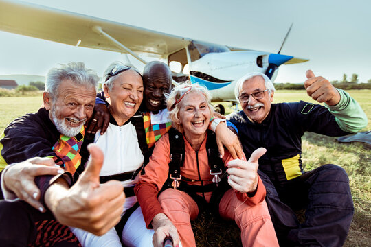 Diverse senior friends taking group photo after skydiving