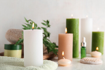 Burning candles and spa supplies on light background