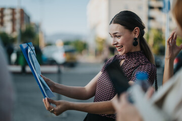 A cheerful woman enthusiastically examines documents during a lively outdoor business meeting in...