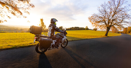 Driver riding motorcycle on empty road during sunset, autumn mountains
