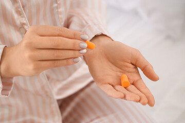 Young woman with ear plugs in bedroom, closeup