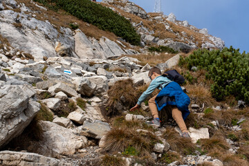 Boy climbing rocky mountain trail with determination on a clear sunny day. Adventure, exploration,...