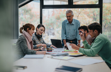 A group of university students engage in collaborative work on a project with guidance from their senior professor, fostering teamwork and learning in a supportive educational environment.