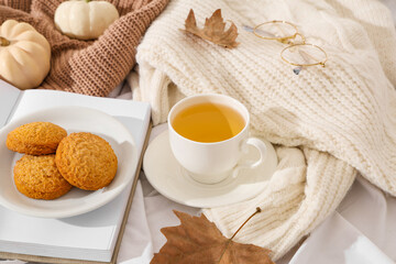 Composition with cup of green tea, cookies, autumn leaves and sweaters on white fabric as background