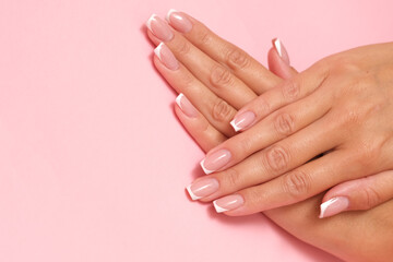 Fototapeta premium Beautiful feminine hands with French manicure on pastel pink background.