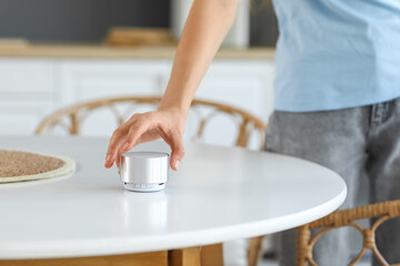 Beautiful young woman with wireless portable speaker in kitchen at home, closeup