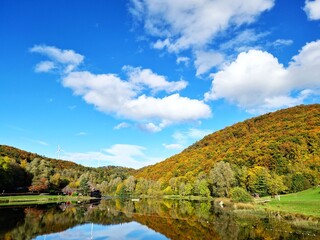 Ein See vor einem bewaldeten Berg mit bunten Bäumen im Herbst an einem sonnigen Tag