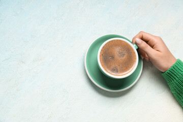 Female hand with cup of coffee on light blue background