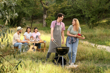 Young friends cooking food on grill at barbeque party