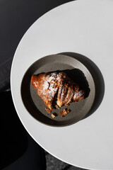 A flaky, golden croissant on a minimalist plate sitting on a modern table in bright sunlight, perfect for a cozy morning