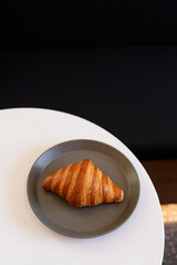 A freshly baked croissant sitting on a grey plate on a white table in a cozy indoor setting during brunch hours