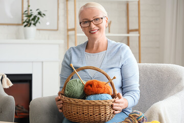 Mature woman with basket of knitting yarn sitting in armchair at home