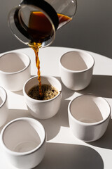 Pouring freshly brewed coffee into white cups during a bright morning in a minimalist kitchen setting