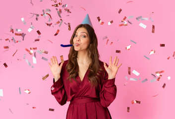 Portrait of excited young lady celebrating birthday standing under confetti rain with cone hat and...
