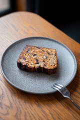 Freshly baked slice of banana bread on gray plate served with a fork on wooden table in cozy café setting