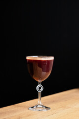 Elegant dark cocktail served in a stylish glass on a wooden table against a black background