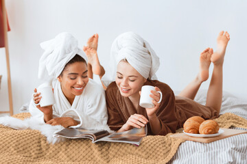 Positive beautiful multiracial girlfriends in bathrobes and towels on heads drinking coffee with...