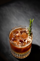 Refreshing cocktail in a glass with ice and a sprig of rosemary served on a dark surface during evening relaxation