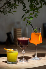 Three colorful cocktails on a wooden bar counter, showcasing vibrant drinks during a relaxed evening gathering