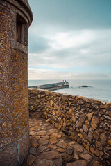 Ancient stone fortress wall and lighthouse pier at Porto harbor under moody sky, Portugal
