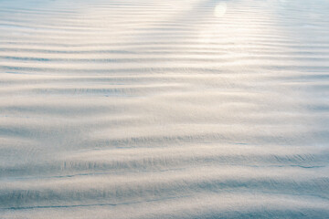Horizontal wave patterns in white beach sand with the sun casting light across the patterns—photo taken at close-up macro. A graphic resource, creative design, surfaces, and backgrounds.
