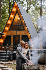 Couple grilling skewers together, enjoying barbecue in forest setting with firewood and nature