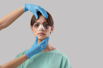 Surgeon hands touching woman's bandaged nose after plastic surgery on grey background