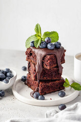 Stack of chocolate brownies with glaze, fresh berries and mint on white plate on white background...
