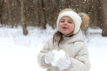 Obraz premium Child girl bite ice cube of snow in park. Little girl eating snow ice outdoors in winter day. Kids cold and flu concept.