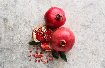 Fresh ripe pomegranates with seeds and leaves on grey background