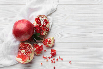 Fresh ripe pomegranates with seeds and leaves on white wooden background