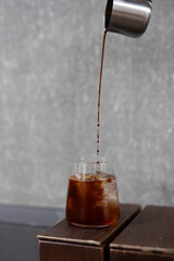 Pouring fresh cold brew coffee into a glass on a wooden table in a minimalist cafe setting