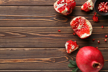 Fresh ripe pomegranates and bowl with seeds on wooden background