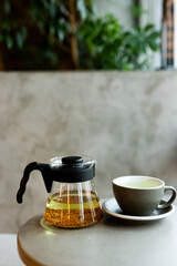 Enjoying a warm cup of herbal tea in a cozy café setting during the afternoon with a glass teapot and a serene atmosphere