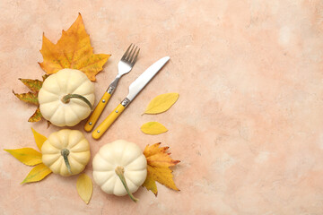 Stylish cutlery with autumn leaves and fresh pumpkins on beige background