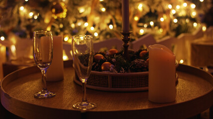 Two empty champagne glasses are standing on a coffee table, illuminated by the warm light of christmas decorations. A romantic new year's eve scene