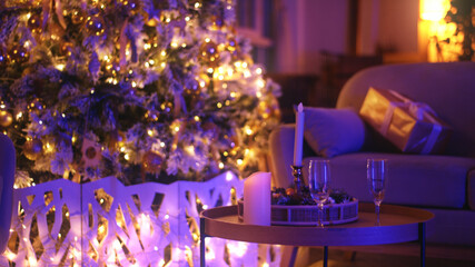Two champagne glasses are standing on a coffee table with a christmas tree in the background, suggesting a festive atmosphere for christmas eve