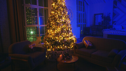 Decorated christmas tree illuminating a modern apartment living room with blue light coming from the windows at night