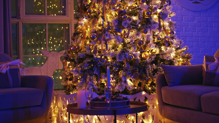 Decorated christmas tree is standing in a living room with its warm lights glowing in the dark. Presents are waiting to be unwrapped under the tree