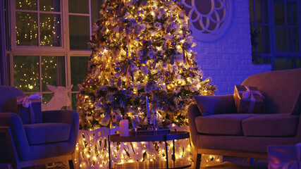 Decorated christmas tree with warm lights is illuminating a cozy living room with wrapped gift boxes placed on armchairs