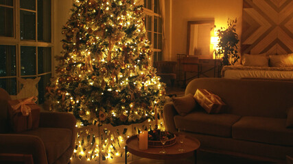 Decorated christmas tree illuminating a cozy living room at night with gifts on armchairs and a view of the city through the window