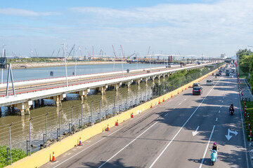 Modern Urban Highway alongside Elevated Transit Bridge over water with construction develpment or Maritime Industrial Zone with port cranes in the distance. Macao, China