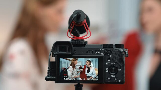Rear view behide camera screen display two women influencer shoot vlog video review clothes prim social media or blog. Girls with apparel studio lighting for live streaming marketing recording session