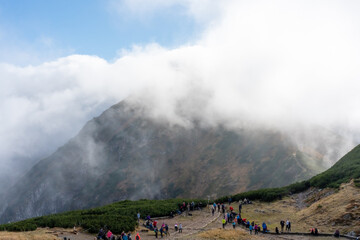 Hikers enjoying mountain plateau with scenic views and low-lying clouds under a bright sky. Concept of nature exploration, group adventure, and outdoor recreation in a breathtaking mountain landscape.